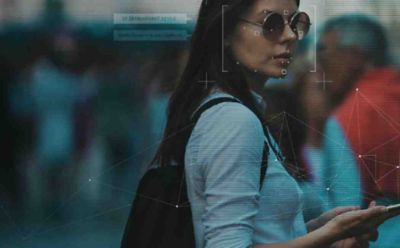 Long-haired woman in sunglasses holding mobile phone, Self-sovereign Identity (SSI) in everyday use | DXC Technology
