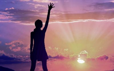 Woman reaching up gazing at brilliant sunset