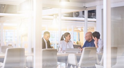 Corporate business meeting in modern office with glass walls, flare from the sunlight and reflections on the glass while business discussions take place amongst board members.