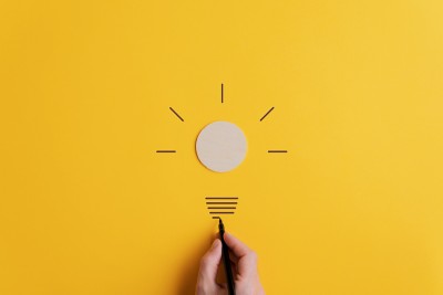 Light bulb made in combination of drawing with black marker and wooden cut circle in a conceptual image of vision and idea. Over yellow background.