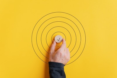 Male hand placing a wooden cut circle with check mark on it in the middle of drawn circles over yellow background.