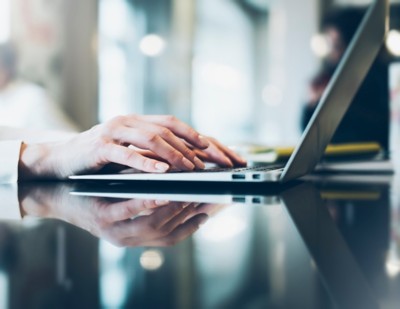 Young woman writing text hands on the open laptop in a cafe on a table with reflection and glare , businesswoman working on computer