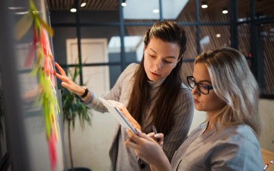 Two women at a whiteboard using sticky notes to plan.