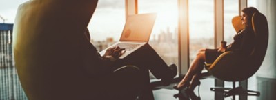 Silhouettes of two business partners sitting in front of each other on curved yellow armchairs on the top floor of a luxurious office skyscraper in front of the window with evening cityscape outside