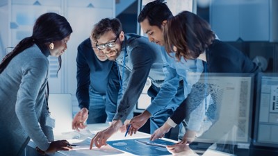 Engineers at illuminated table in a planning meeting.