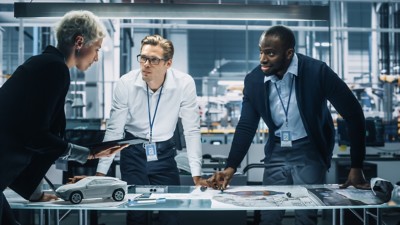 Young Diverse Team of Automotive Engineers Working in Office at Car Factory. Industrial Designer Talks About Electric Engine Parts with Colleagues, Discussing Different Technological Applications.