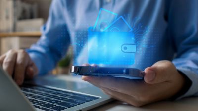 Man in blue shirt at laptop holding a phone with digital wallet, banking in a data-rich world | DXC Technology Insights