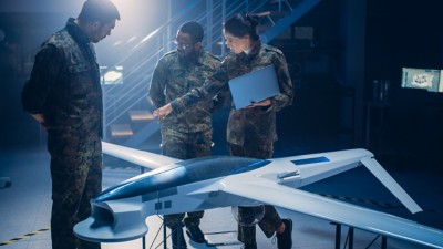 Three army technicians in a lab discussing a drone prototype, Aerospace & Defense | DXC Technology