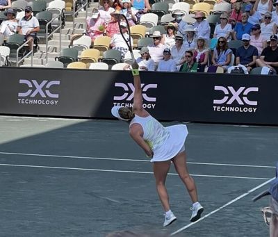 Tennis player reaching to hit the ball with DXC logo in background