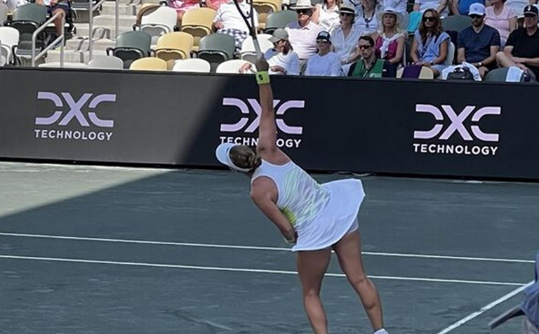 Tennis player reaching to hit the ball with DXC logo in background