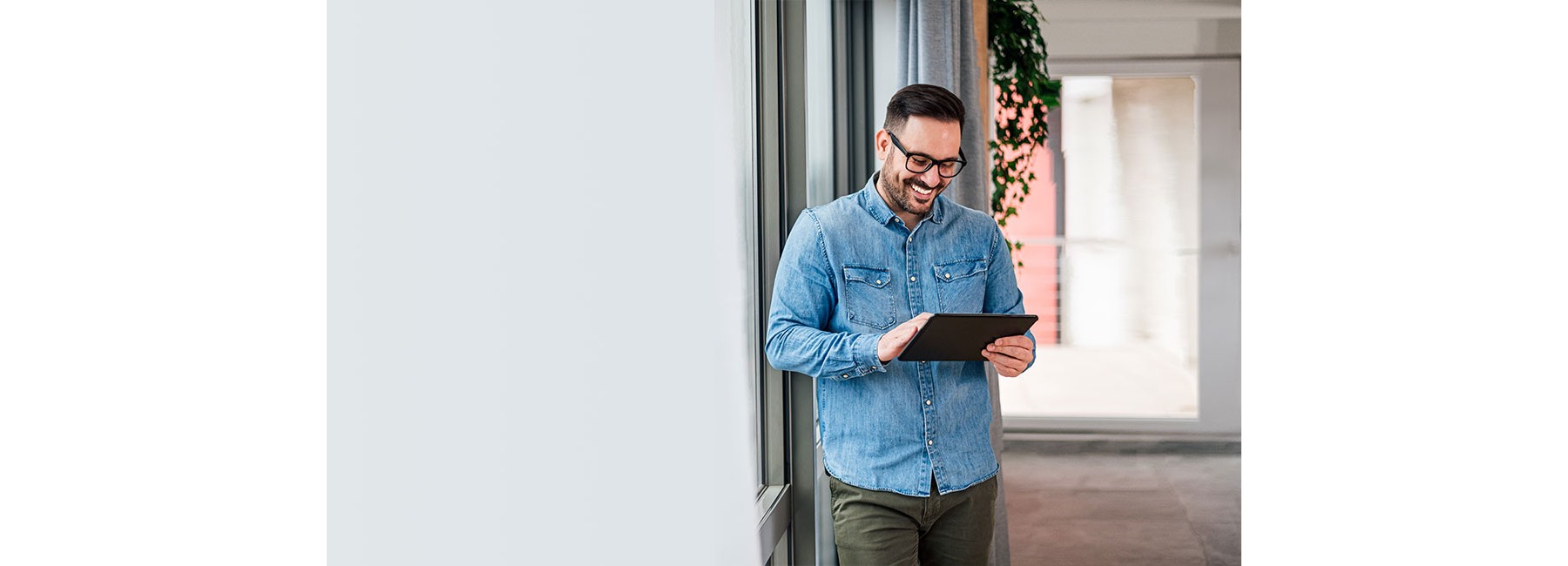 Smiling man businessman in casuals standing in office next to window using tablet making online shopping purchasing Small business home office entrepreneur looking at tablet making online video call