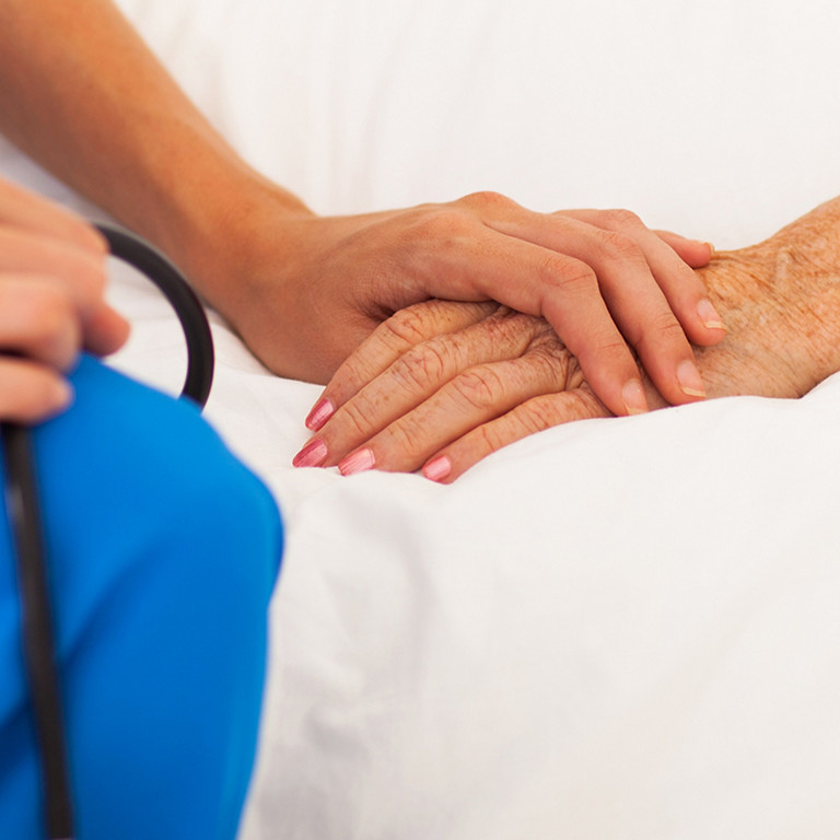 medical doctor holing senior patient's hands and comforting her