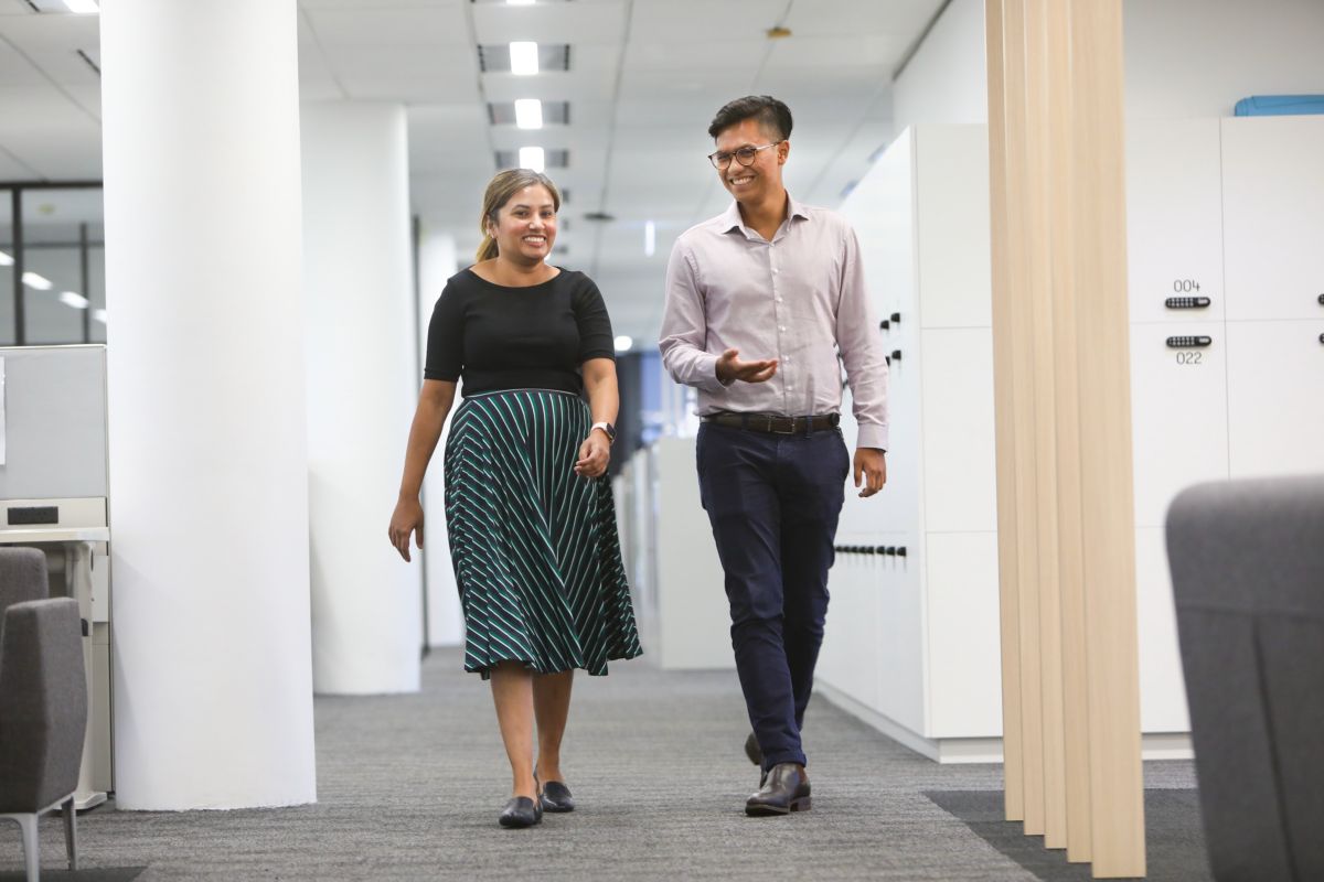 Two colleagues walking and talking in an office hallway