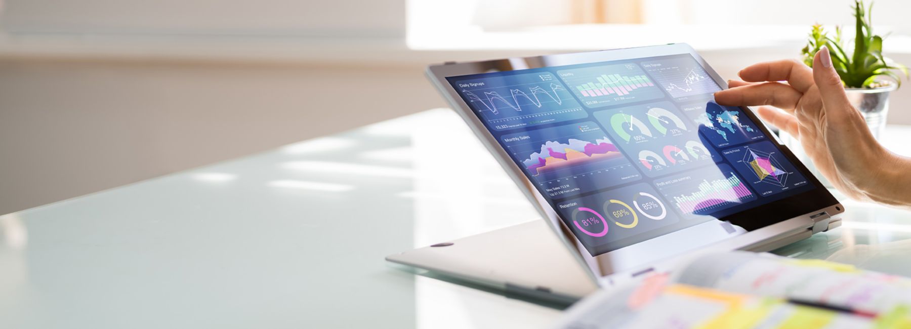 Woman's hand on touchscreen tablet showing colorful data, charts and graphs in bright office, Data & AI | DXC Technology
