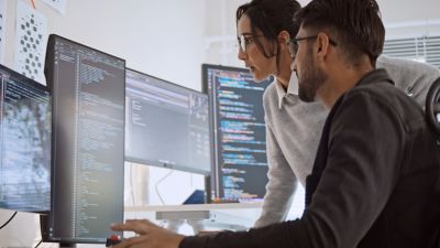 Male and female SAP programmers looking at code on a screen; Migrate to RISE with SAP S4/HANA in less than 12 months | DXC Technology