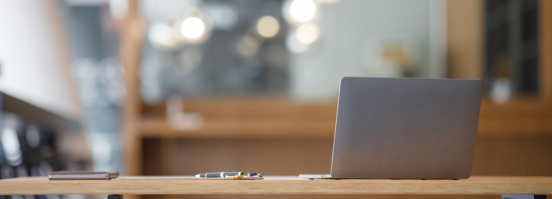 Laptop, notebook, and eyeglasses sitting on a desk in a large open office space, UK&I Academic Programme | DXC Technology