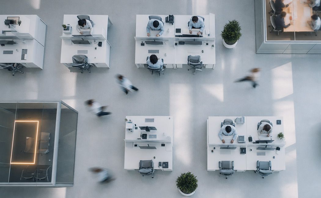 Overhead view of a bright, modern open-plan office with people working at white desks and blurred figures walking past