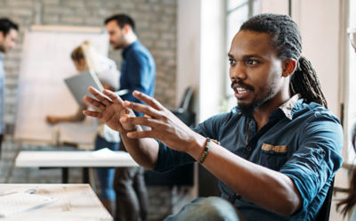 man gesturing at computer screen with intent and energy, with others