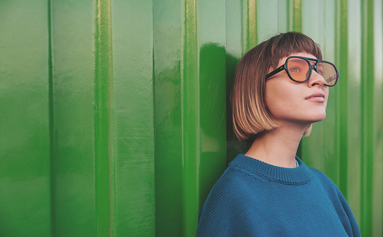 woman looking away through sunglasses standing on green wall background